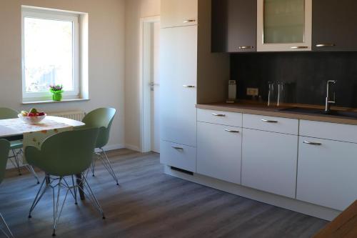 a kitchen with white cabinets and a table with green chairs at Ferienwohnung Hof Margarethental in Goldelund