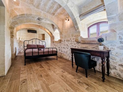 a bedroom with a bed and a desk in a stone wall at Luxury Farmhouse Villa surrounded with Nature & Farm Animals Alpacas etc in Għasri