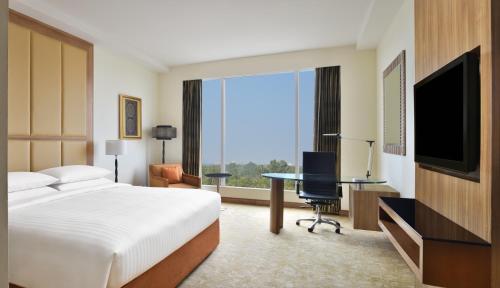 a hotel room with a bed and a desk and a television at Bengaluru Marriott Hotel Whitefield in Bengaluru