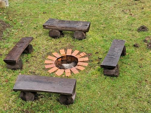 three wooden benches and a fire pit in the grass at Chata Mezičky in Jiřetín pod Jedlovou