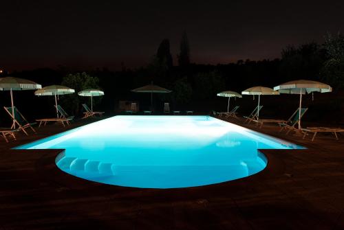 a blue pool with chairs and umbrellas at night at Antiqua Vallis in Palaia