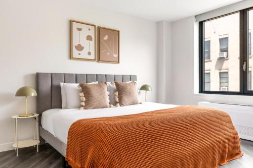 a white bedroom with a large bed with an orange blanket at E Village 1BR w WD Elevator Gym NYC-889 in New York