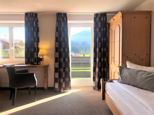 Schlafzimmer mit einem Bett, einem Schreibtisch und einem Fenster in der Unterkunft Sonnenbichl Hotel am Rotfischbach in Fischen im Allgäu