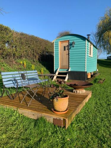 ein kleines grünes Haus mit einem Tisch und einer Bank in der Unterkunft The Gannah Farm Shepherds Hut in Hereford