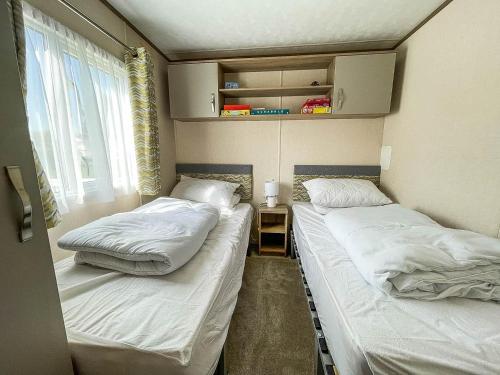 2 camas individuais num pequeno quarto com uma janela. em Beautiful 6 Berth Caravan At Breydon Water Nearby Great Yarmouth Ref 10056b em Belton