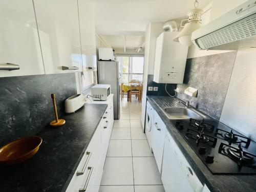 une cuisine avec des armoires blanches et des comptoirs noirs dans l'établissement Appartement spacieux à Cap d'Agde, proche port, commodités et plage, parking inclus - FR-1-723-10, au Cap d'Agde