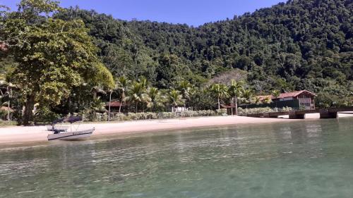 a boat in the water on a beach with trees at Apartamento em Chácara Aconchegante in Angra dos Reis