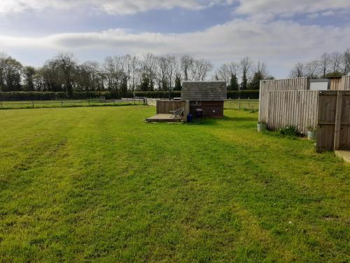 a large grassy field with a fence and a shed at Glamping in Wiltshire the Green Knoll is a charm in Chippenham
