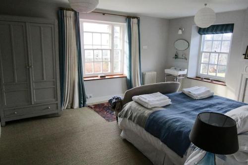 a bedroom with a bed with blue sheets and two windows at Wolford Lodge Traditional home surrounded 150 private acres with Tennis court in Honiton