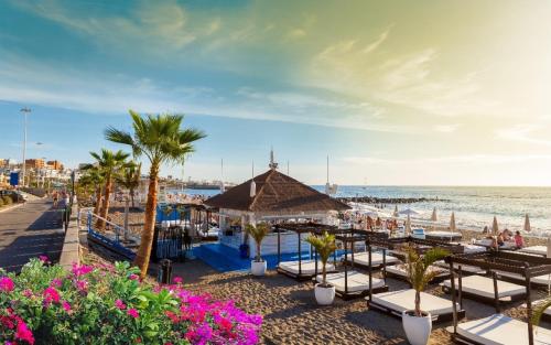 una playa con mesas, sillas, palmeras y el océano en Apartments Las Brisas Costa Adeje en Adeje