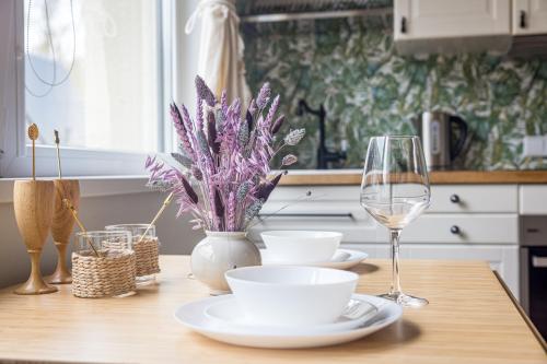 a table with plates and glasses and a vase with purple flowers at Apartamentai Čiki puki 2 aukštas in Palanga