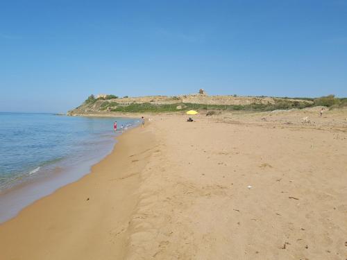 a beach with a yellow umbrella and the ocean at Hotel Admeto in Marinella di Selinunte