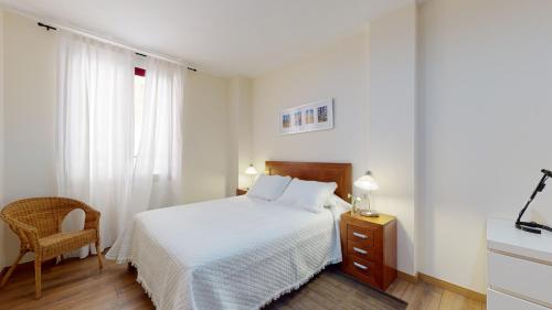 a white bedroom with a bed and a chair at Edificio Galerias in Lorca