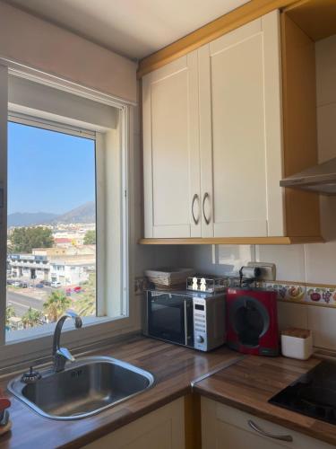 a kitchen with a sink and a microwave and a window at Piso primera línea, Banana Beach, Marbella. in Marbella