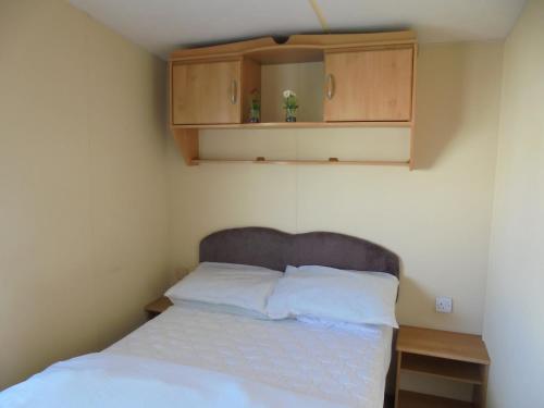 a bedroom with a bed with white sheets and wooden cabinets at 6 Berth heated on The Chase (Albany II) in Skegness