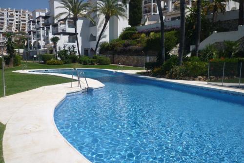 ein großer blauer Pool mit Palmen und Gebäuden in der Unterkunft Golf views 2 bed El Mirador De Calahonda in Mijas Costa