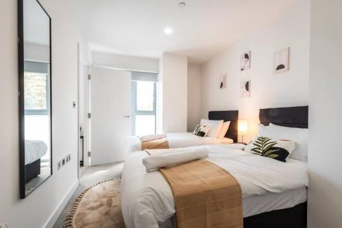 a white bedroom with two beds and a tv at Saffira - 2 bedroom Flat in Bracknell