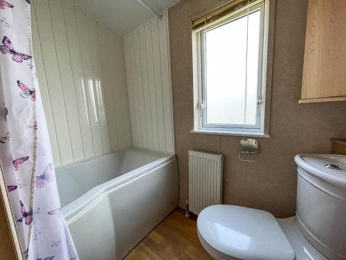 a bathroom with a tub and a toilet and a window at Lovely 6 Berth Caravan With Decking At California Cliffs In Scratby Ref 50048l in Great Yarmouth