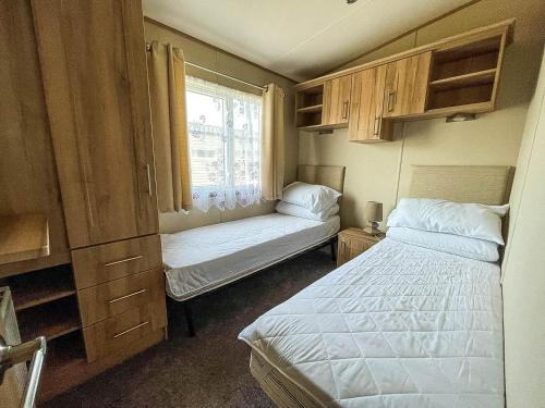 a small bedroom with two beds and a window at Beautiful Caravan With Sea Views At California Cliffs In Scratby Ref 50010oc in Great Yarmouth