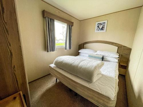 a bedroom with a bed with white sheets and a window at Lovely Caravan With Decking And Free Wifi In Lowestoft Ref 12106b in Lowestoft