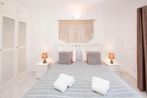 a white bedroom with a large bed with pillows at Windmill by OCvillas in Albufeira