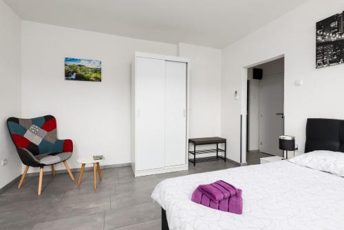 a white bedroom with a bed and a chair at Studio apartman Sirius in Slunj