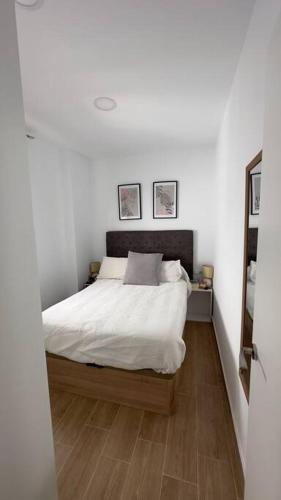 een slaapkamer met een bed met witte lakens en een houten vloer bij Rockside Residentes Suites La Línea N5 in La Línea de la Concepción