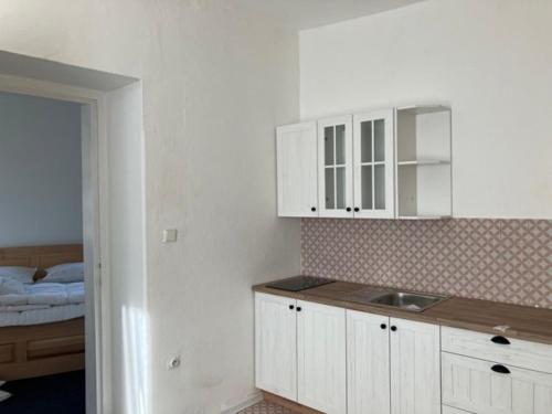 eine Küche mit einem Waschbecken, weißen Schränken und einem Bett in der Unterkunft Apartmány Windy in Staré Město