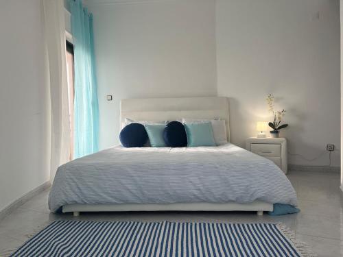 a white bedroom with a large bed with blue pillows at O mar na frente de lux Caparica in Costa da Caparica
