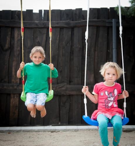 two children sitting on swings in a playground at Apartmány u Dlouhána in Kadaň
