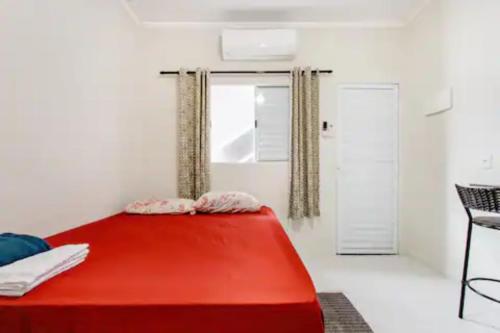 uma cama vermelha num quarto branco com uma janela em Pousada Casa da Fernanda, Suíte Moon na Praia Grande