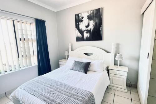 a white bedroom with a bed and a window at Stylish Hartenbos Apartment in Mossel Bay