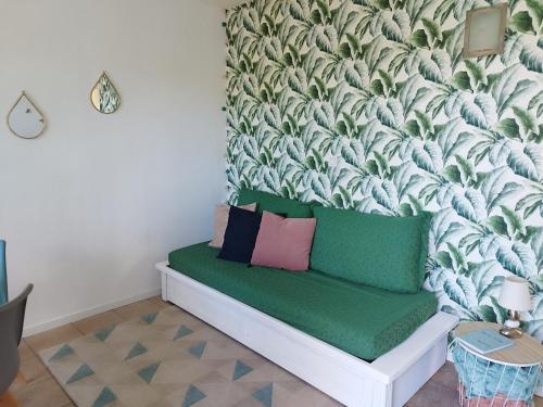 a room with a green couch with a tropical wallpaper at Le petit jazz du lac in Marciac