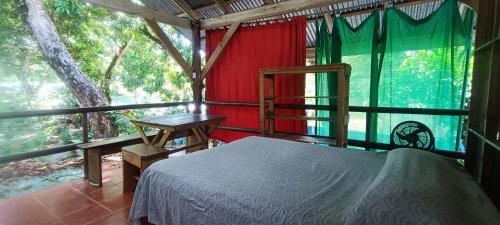 a bedroom with a bed and a table and a window at Flutterby House Hostel in Uvita
