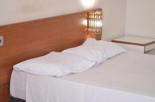 uma cama branca com uma cabeceira em madeira e almofadas brancas em Tuti Bororô em Rondonópolis