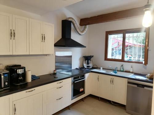 une cuisine avec des armoires blanches et un comptoir noir dans l'établissement La Taurelle, Maison T3 climatisée avec terrasse au cœur de Gallargues-le-Montueux, à Gallargues-le-Montueux