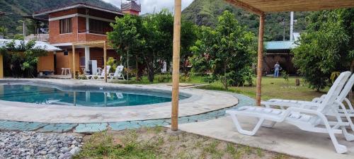 a pool with two white chairs and an umbrella at Pampa Bella Lodge in La Merced
