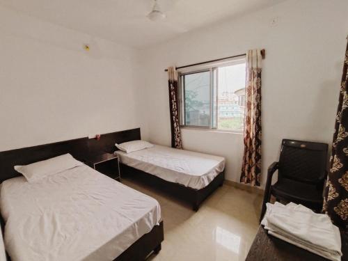 Un dormitorio con dos camas y una ventana y una silla. en Dwarka Home Stay, en Bodh Gaya