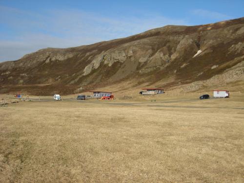 a field with cars parked in front of a mountain at Ásbrandsstadir Cottage in Vopnafjörður