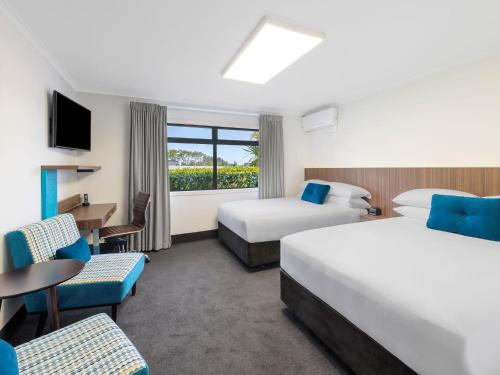 a hotel room with two beds and a table and chairs at JetPark Hamilton Airport New Zealand in Hamilton