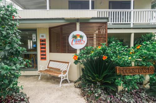 a bench outside of a restaurant with a sign and flowers at The Cooks Oasis in Rarotonga