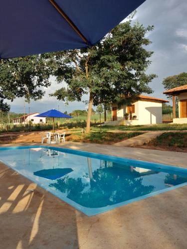 a blue swimming pool with a table and an umbrella at Chalés por do sol in Pirenópolis