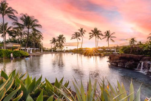 a pond with palm trees and a sunset in the background at The Lodge at Kukuiula - CoralTree Residence Collection in Koloa