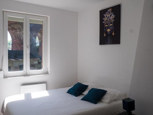 a white bed with blue pillows in a room with a window at Maison de ville Rouen Darnétal in Darnétal