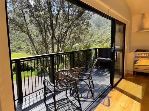 a balcony with two chairs and a large window at Ruruwai - Piha in Piha
