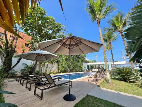 a patio with two umbrellas and chairs and a pool at SAL di Mare Hotel Boutique - Frente ao Mar com Piscina in Guarujá