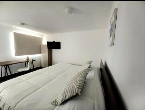a bedroom with a large white bed and a desk at Hotel Tabancura in Copiapó