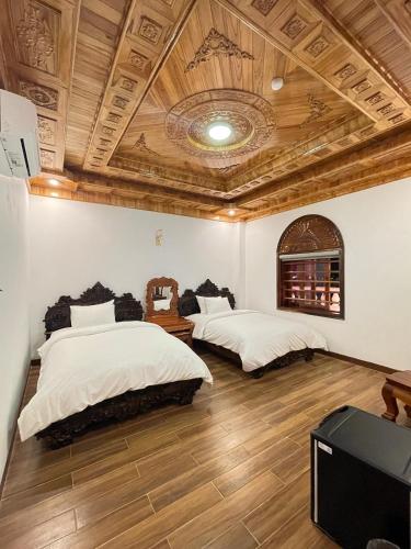 Duas camas num quarto com tectos em madeira e pisos em madeira em Hotel Hoàng My em Pleiku