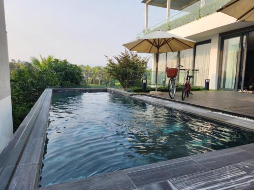 a swimming pool with an umbrella next to a house at FLAMIGO ĐẠI LẢI RESORT - Villa View Hồ in Ngọc Quang