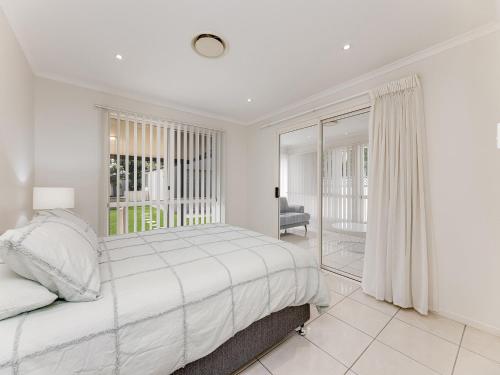 a white bedroom with a bed and a chair at 11 Wills Avenue Golden Beach QLD in Golden Beach